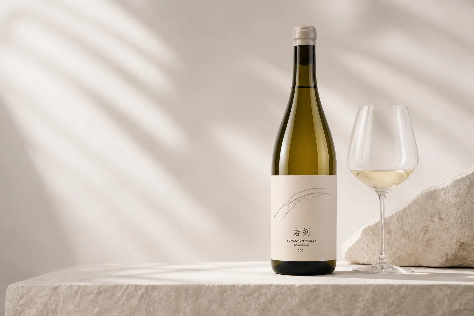 Yanker Chardonnay bottle with a wine glass beside a pale stone block in a restrained studio setting