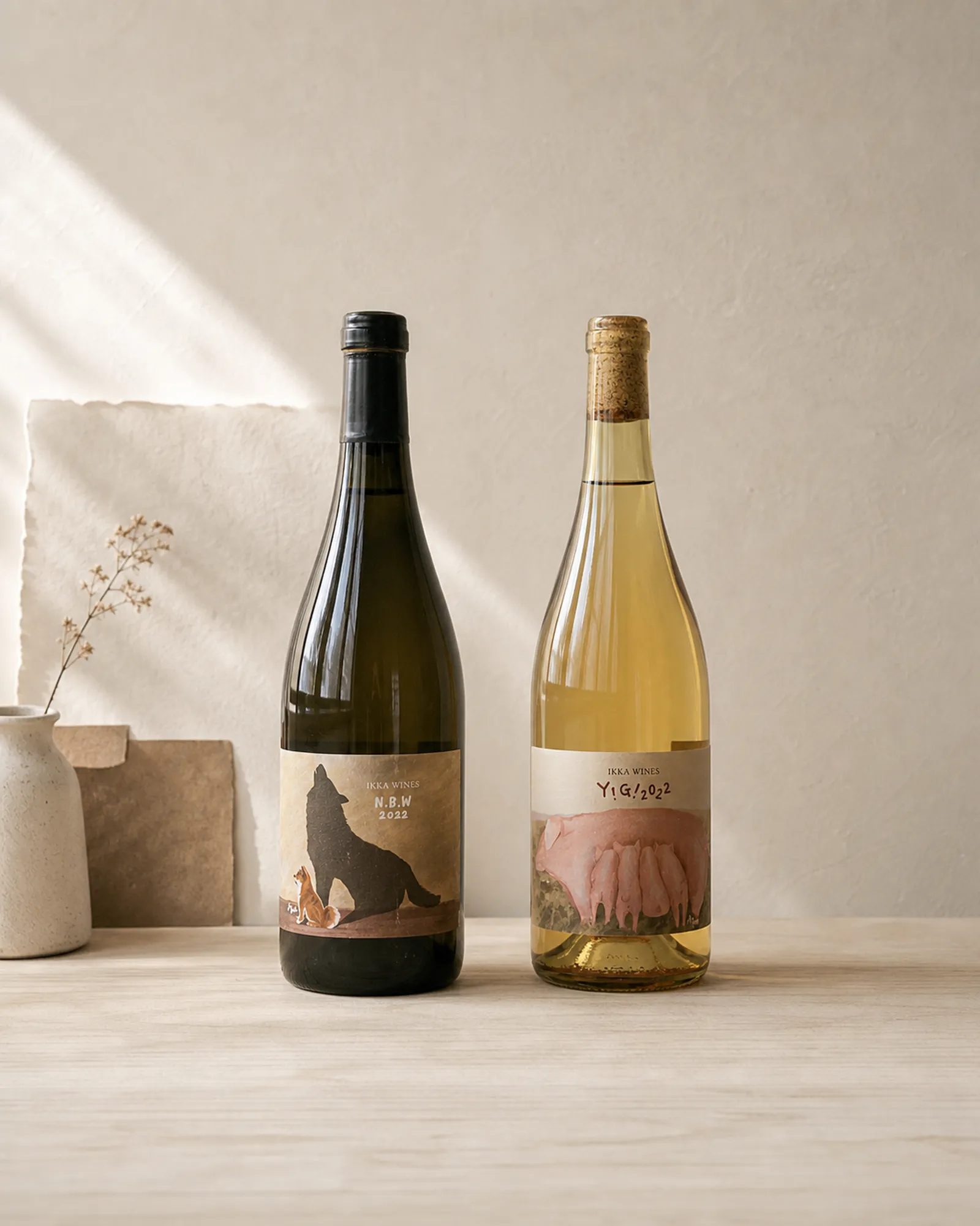 Full-bottle study of IKKA WINES animal labels in a quiet natural-light studio with the N.B.W dog silhouette and Y!G! pig group