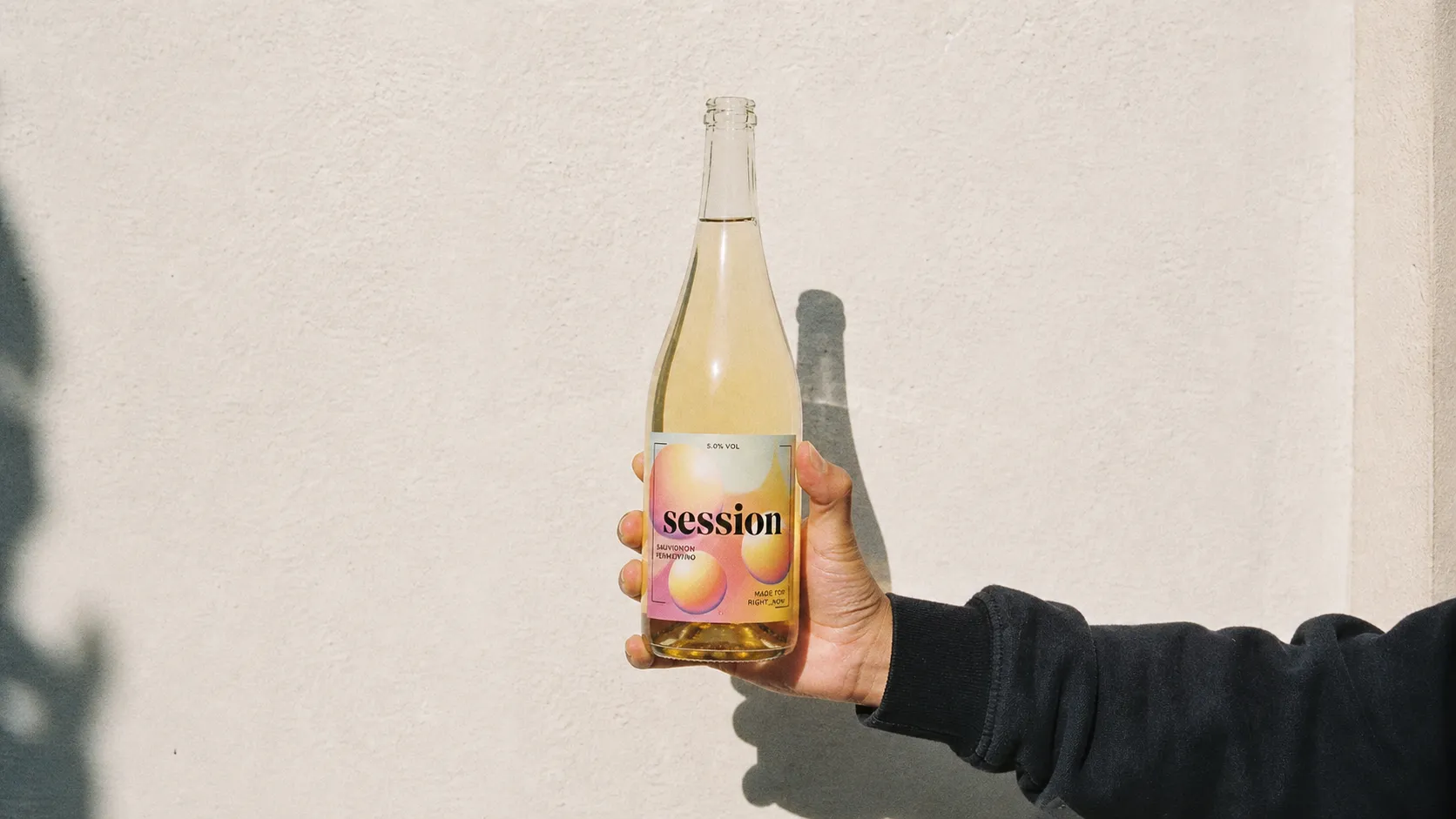 SESSION WINE bottle held fully against a pale plaster wall in hard afternoon sun